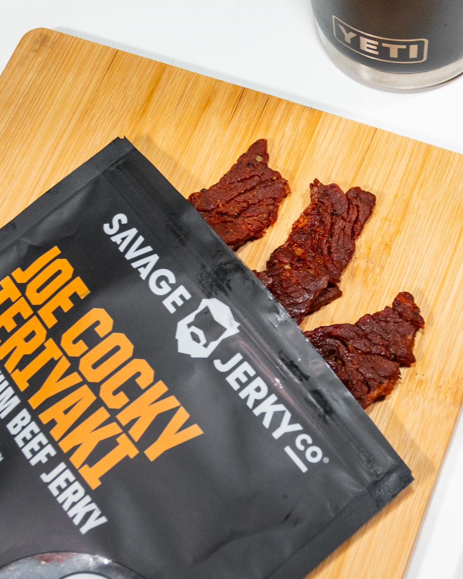 Savage Jerky Co. teriyaki beef jerky on a cutting board with a YETI mug in the background.
