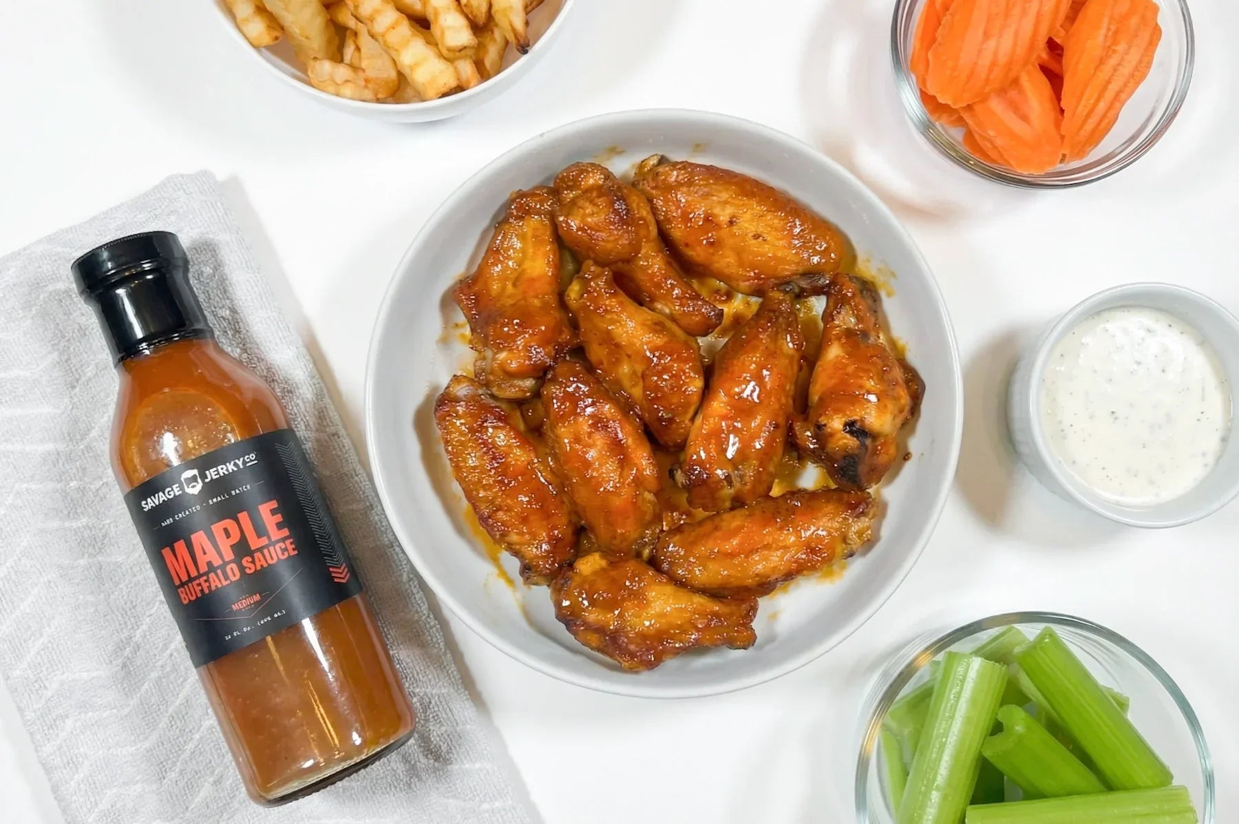 maple buffalo chicken wings surrounded by french fries, carrots, celery and ranch dressing.